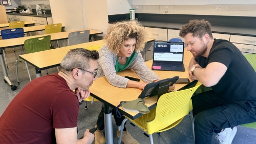 3 people look at a tablet in a classroom