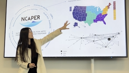 Presenter with long black hair discussing the arts across the US map