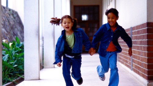 Two young girls run in a school corridor
