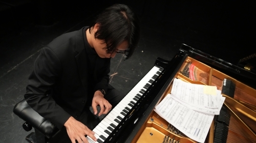 Above shot looking down on student playing piano with paperwork on top of piano