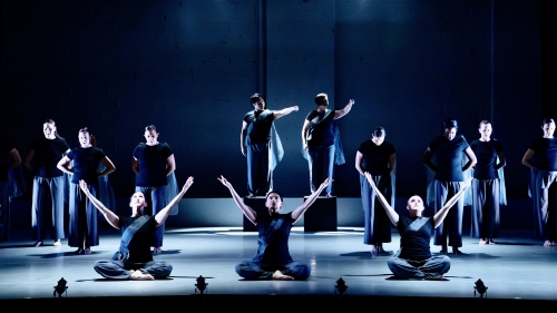 A deep blue stage with dancers posed, some on the floor and some standing