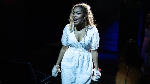 Sole singer on dark stage in white dress performing song