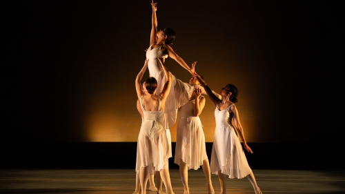 Dancers in all white holding up single dancer