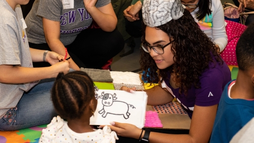 A student shows a young child a picture of a cow