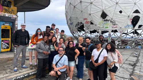 A smiling group of teachers stands in front of a radar dome covered in graffiti