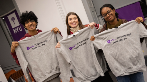 Three students hold up sweatshirts that say NYU Steinhardt SURE Fellow 