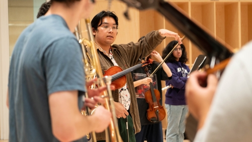 Sam Wu speaking to a rehearsal room of musicians, holding instruments
