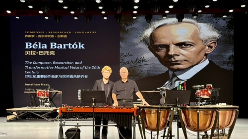 Two men standing behind perdussion instruments on stage in front of large artist headshot