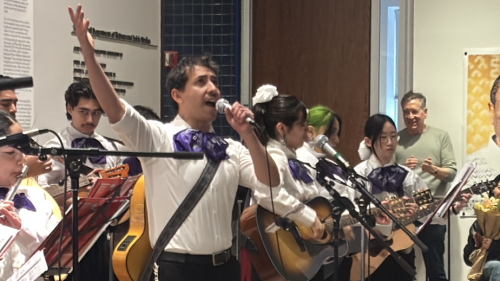 Mariachi performing with lead singer lifting one arm up in the air in celebration