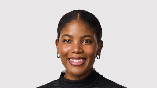 A young black woman with hair in a bun smiles at the camera. She is wearing a black turtleneck and small hoope earrings. 