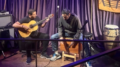 Two men playing instruments, a guitar and drum