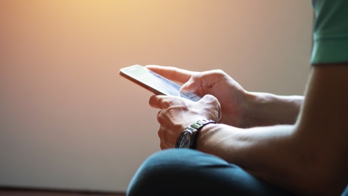 A person sits cross-legged on the floor looking at their smartphone.