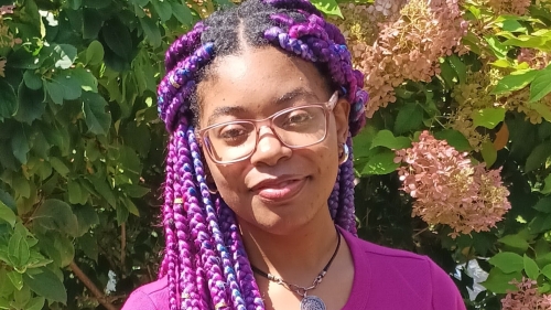 Photo of Madison wearing a pink shirt, green foliage and flowers in background