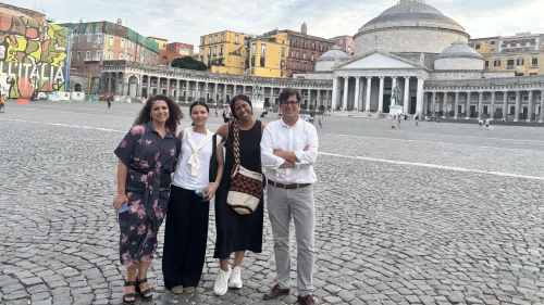 Four researchers and scholars pose for a photo in a stone-paved plaza in Italy. 
