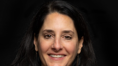 Headshot of Mary Helen Immordino-Yang smiling, wearing a black collared top, long earrings, and a necklace against a black background.