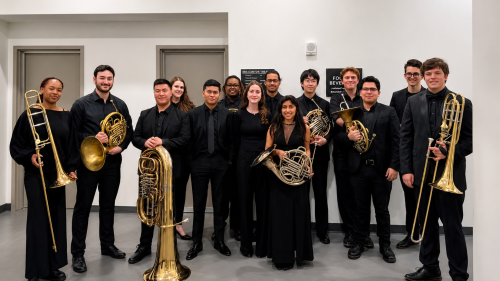 Brass Studies students posing for group photo before concert. Dressed in black and holding instruments.