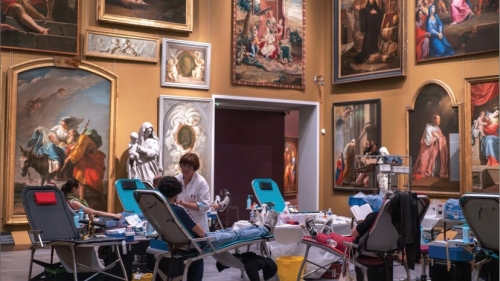 People lay down on blood donation chairs inside a museum.