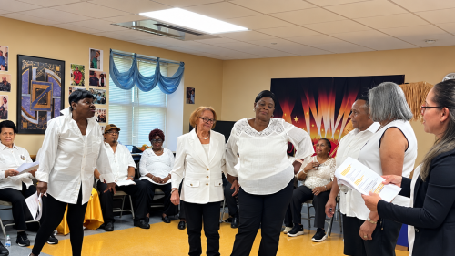 Six Breaking Ground resident drama therapy participants stand and rehearse while a circle of others sit and watch