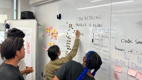A group stands at a whiteboard and writes on the board