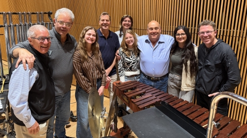 Percussion students posing with faculty in orchestra venue setting