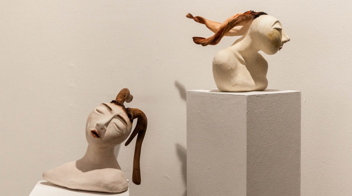 Two ceramic buffs facing in opposing directions, with braided hair floating from each head