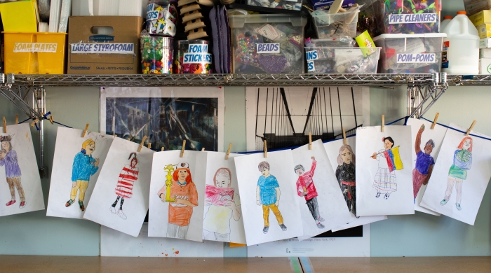 Student artwork hanging on clothespins, with art materials above