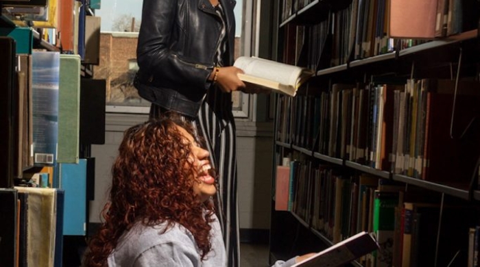 Two Counseling@NYU students read books in the library.