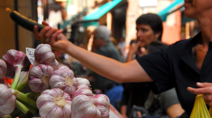 shoppers at a food market, with bulbs of garlic in the foreground