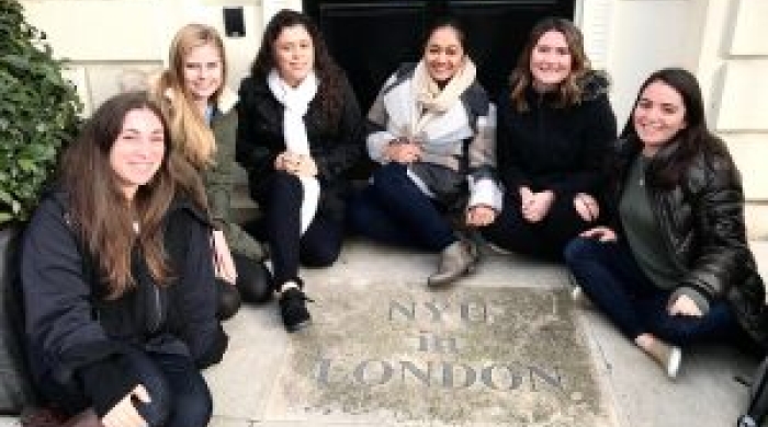 Students sitting around a plaque that reads "NYU in London"
