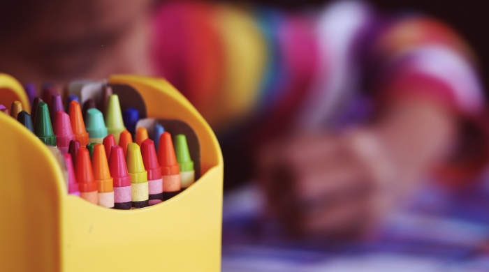 Crayons with a coloring child in the backgroun
