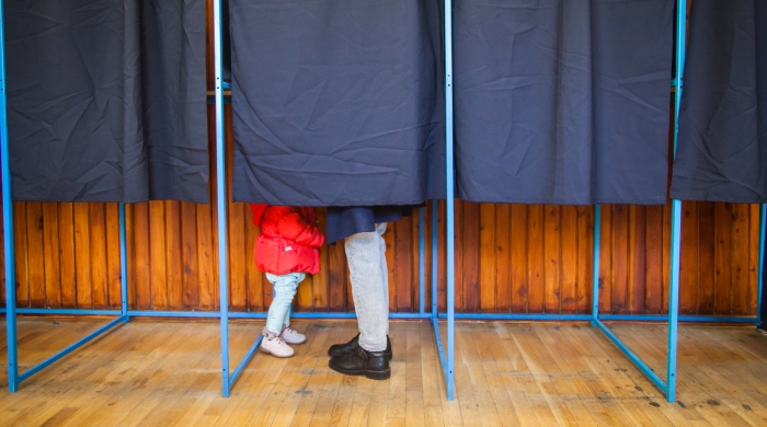 A photo of voting booths with the feet of a parent and child visible