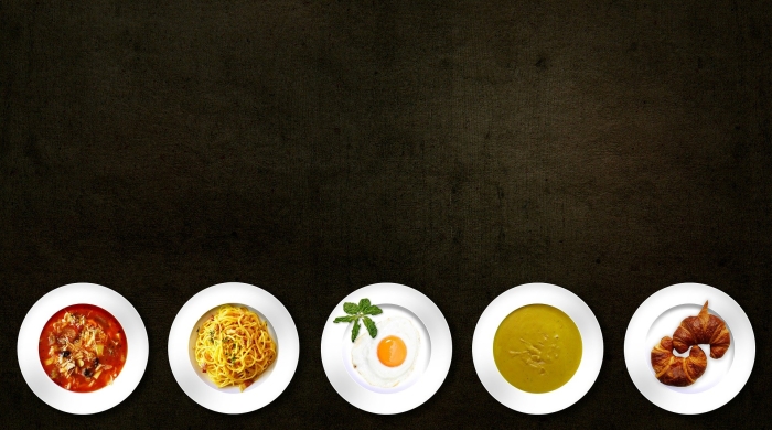 An overhead shot of various plates of pasta, eggs, soup, and croissants.