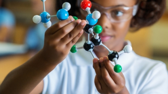 A young girl holds up a 3-D model of an atom.