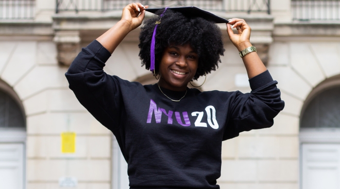 Kyra wearing an NYU20 shirt and a graduation cap with a violet tassel.