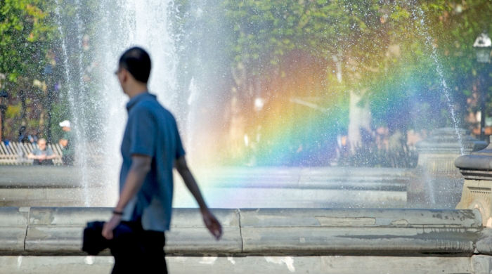 A rainbow appears in the Washington Square fountain as a student passes by