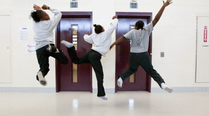 Three girls jumping in celebration in front of doors labelled "D-3 230" and "D-2 229"