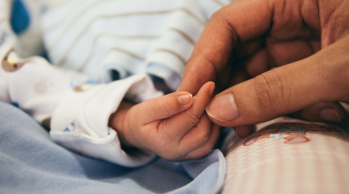 A photo of an adult holding the hand of an infant