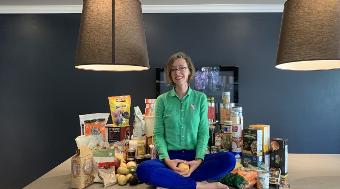 Christy sitting on a table surrounded by pantry food items.