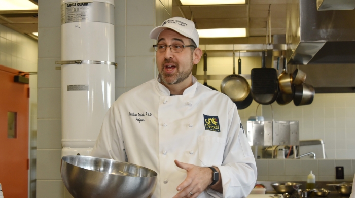 Jonathan Deutsch in a chef's white jacket holding a metal mixing bowl in a kitchen.