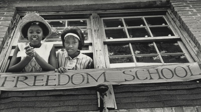 Two young black girls smile and lean out of the window of a freedom school