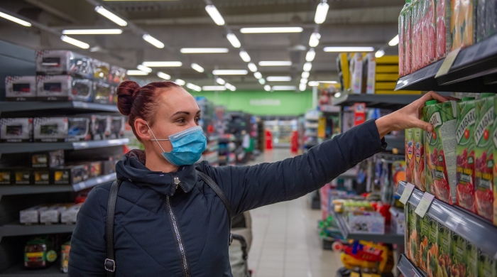 A photo of a woman wearing a face mask and grabbing juice off the shelf of a supermarket