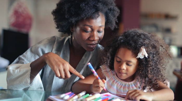 A Black mother and daughter sit together as the daughter colors
