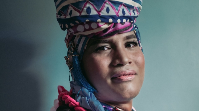 Indigenous gender expansive woman wearing traditional cultural clothing and smiling into the camera