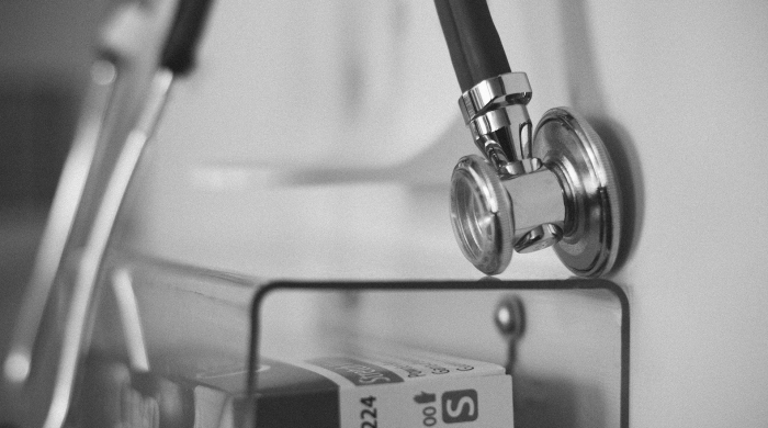 A black and white image of a stethoscope handing over a box of medical gloves.