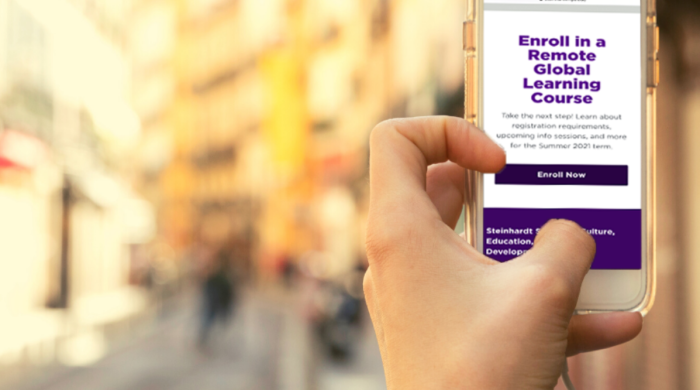 A close up photo of someone holding a phone displaying text that says, "Enroll in a Remote Global Learning Course"
