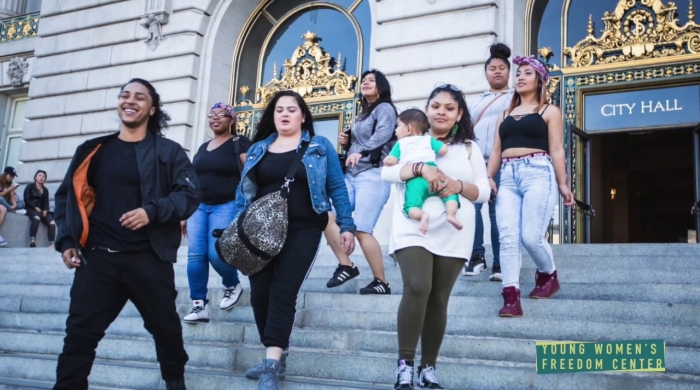 A photo of the Young Women's Freedom Center team walking down the steps in front of a City Hall building with the Young Women's Freedom Center logo in the bottom corner
