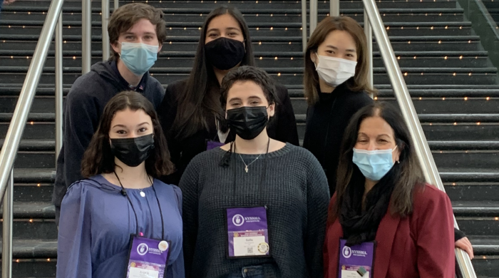 group of 5 students and 1 professor wearing purple name badges pose in front of staircase