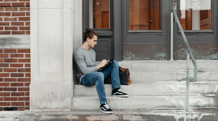 Person sitting on concrete stair leaning on wall.