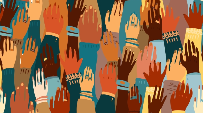 Raised hands of various skin tones and sweater colors. Some hands are adorned with jewelry and some hands are not. 