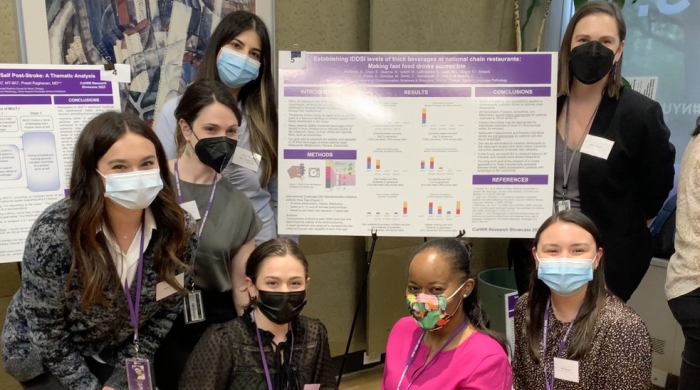 Seven students wearing masks, posing around a presentation board at the CoHRR Spring Showcase
